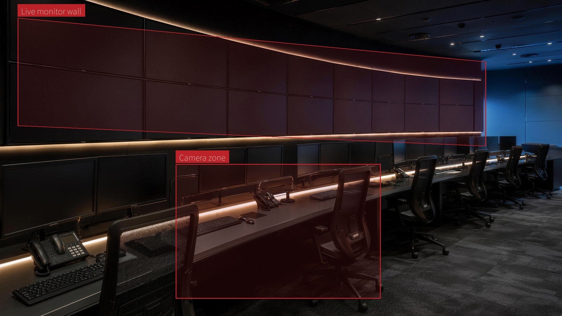 A dark operations room with a curved wall of blank monitors above a long console desk